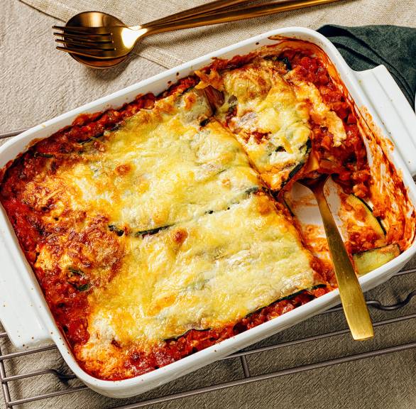 Vegetarische Zucchinilasagne in einer Auflaufform, ein Stück auf einem Teller daneben