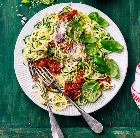 Low-Carb-Zucchinispaghetti angerichtet mit Tomatensoße und Basilikumpesto auf einem Pastateller