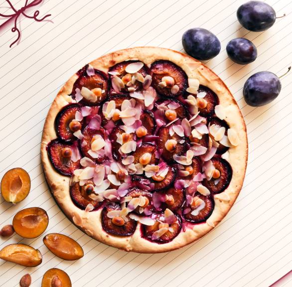 Selbstgebackener runder Zwetschgenkuchen mit Zimttupfen getoppt von Mandelblättchen auf einer Kuchenplatte