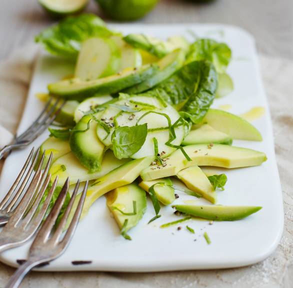 Veganer Avocado-Salat mit Apfel und Basilikum angerichtet mit Limettendressing auf einer Servierplatte