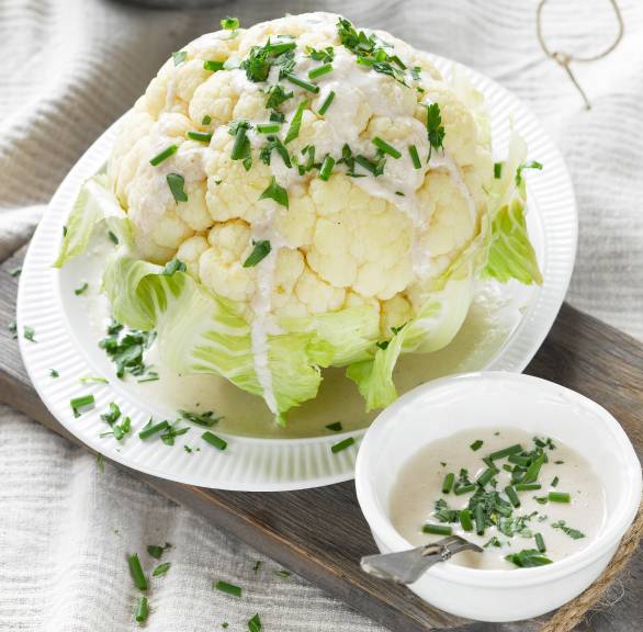 Ganzer, dampfgegarter Blumenkohl auf einem Teller übergossen mit italienischer Mandel-Knoblauch-Soße
