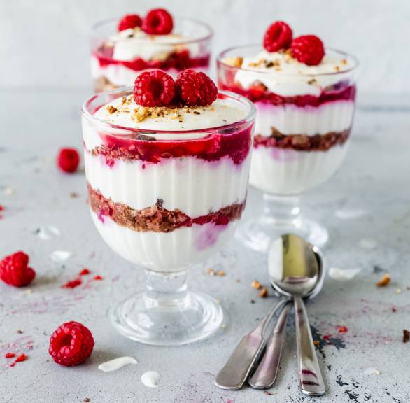 Drei Gläser Dessert im Glas mit Schichten aus Cantuccini und weißer Creme getoppt von Himbeeren