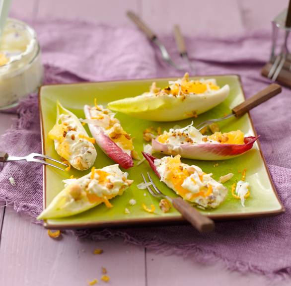 Mehrere Chicorée-Schiffchen gefüllt mit Frischkäse, Orangen und getoppt von Walnüssen auf einer Vorspeisenplatte
