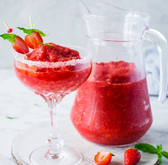 Selbst gemachter, dekorierter Strawberry Margarita in einem Coktailglas, dahinter eine Karaffe mit mehr