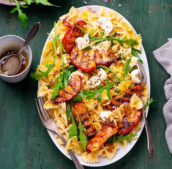 Nudelsalat mit gegrillten Nektarinen, Rucola und Mozzarella angerichtet auf einer Servierplatte