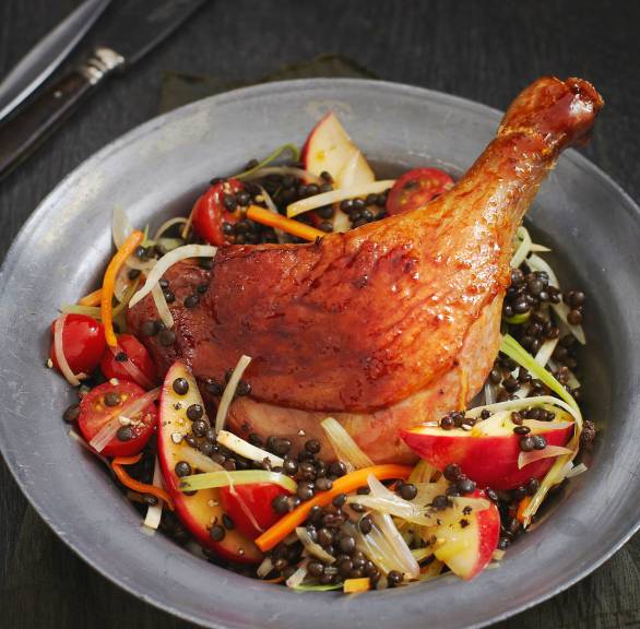 Eine Entenkeule angerichtet auf Linsen-Apfel-Gemüse mit Tomaten auf einem Teller