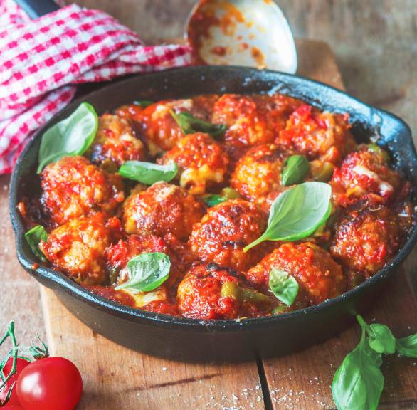 Hackfleischbällchen in Tomatensugo in einer Pfanne auf einem Tisch umringt von frischen Zutaten