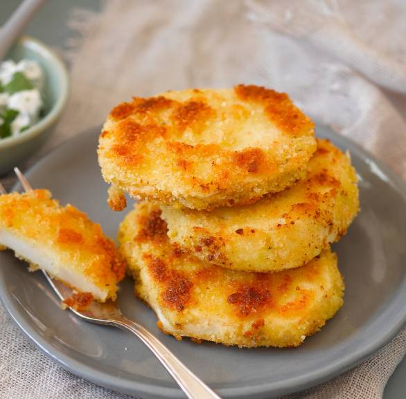 Drei panierte, goldbraune Sellerieschnitzel gestapelt auf einem Teller, daneben ein Dip