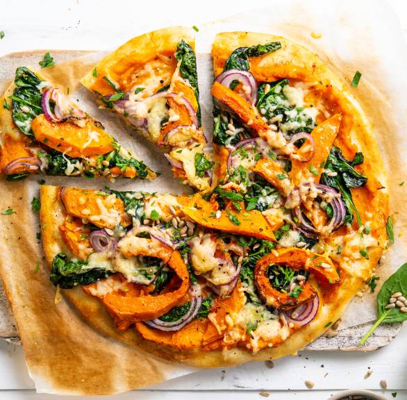 Pizza belegt mit Kürbisspalten, Spinat und Käse angeschnitten auf einem Teller