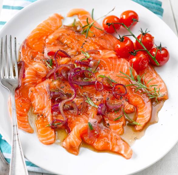Lachscarpaccio auf einem Teller angerichtet getoppt von Tomaten und Kräutern