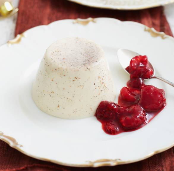Zwei Törtchen Lebkuchen Panna cotta auf Desserttellern, daneben heißen Himbeeren