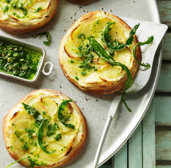 Mehrere Mini-Kartoffelpizza mit Tofu-Soja-Creme und grünem Pesto angerichtet auf einer Servierplatte