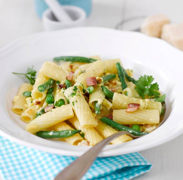 Tortiglioni mit grüner Carbonara mit Bohnen, Erbsen und Speck angerichtet auf einem Teller
