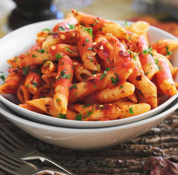 Penne all’arrabbiata in einem tiefen Teller auf einem Tisch, daneben eine Pfeffermühle