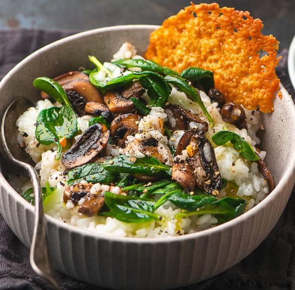 Pilzrisotto in einer Schale mit Spinat und einem runden Parmesanchip
