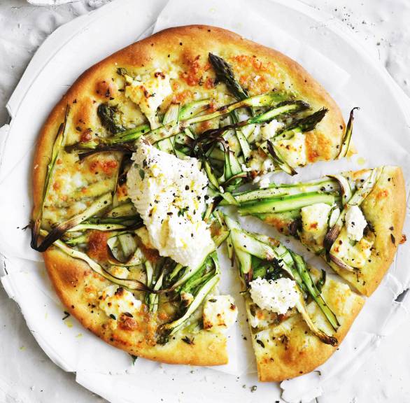 Vegetarische runde Spargelpizza angeschnitten auf einem Teller getoppt mit Ricotta