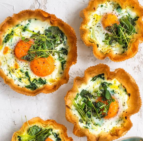 Mehrere selbstgebackene Ricotta-Törtchen aus Filoteig gefüllt mit Ei, Sahne und frischen Kräutern auf einem Tisch