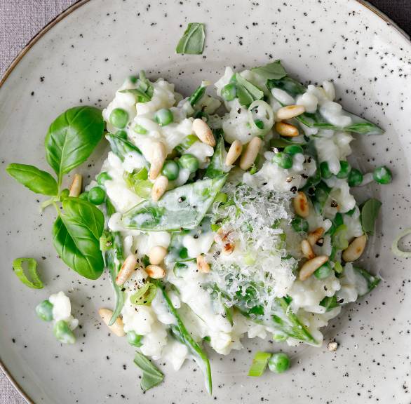 Risotto mit Zuckerschoten, Erbsen und Mascarpone getoppt von Pinienkernen angerichtet auf einem großen Teller