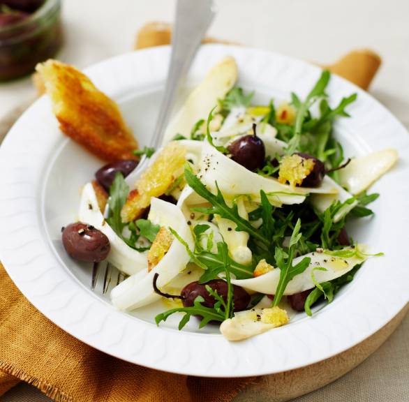 Roher weißer Spargelsalat mit Oliven und Rucola auf einem Teller