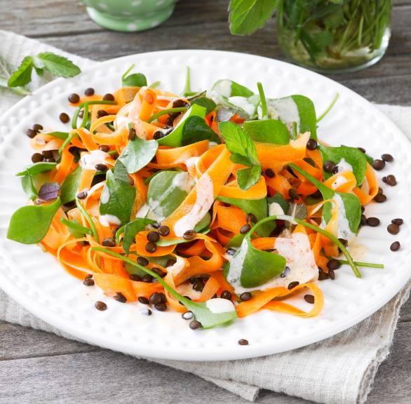 Möhren-Rohkost-Salat auf einem Teller getoppt mit Linsen und Schmand-Dressing