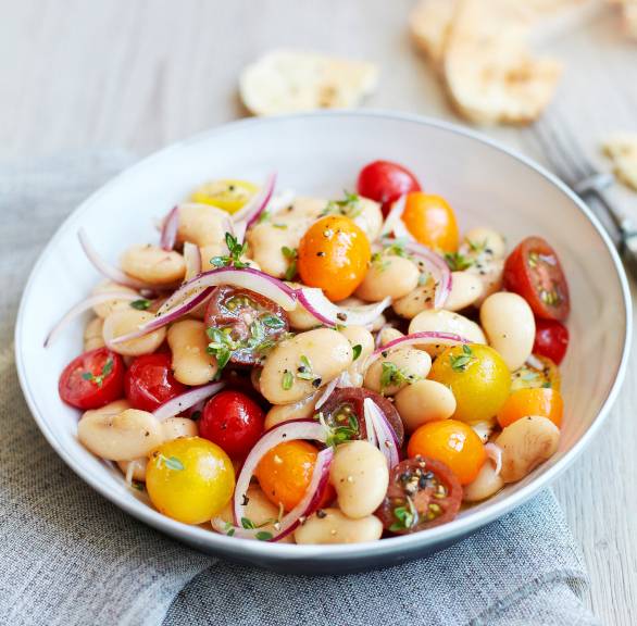 Salat aus weißen Riesenbohnen und Tomaten angerichtet auf einem tiefen Teller