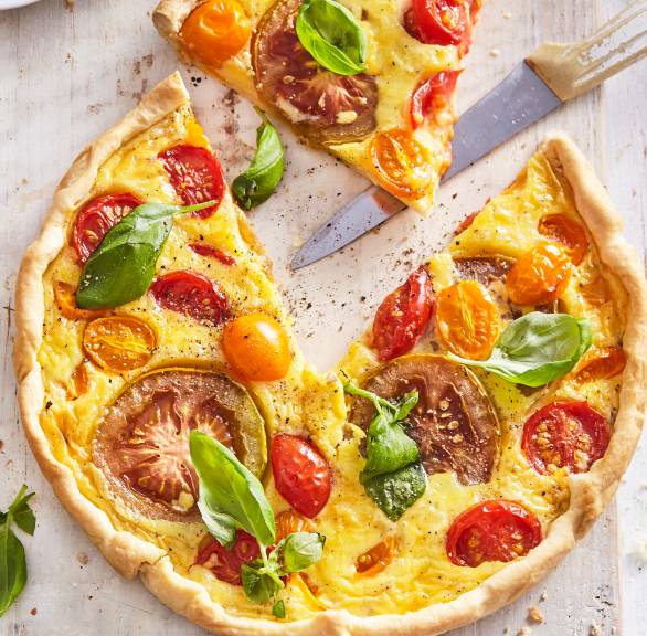 Quiche mit bunten Tomaten, Ricotta und Parmesan angeschnitten auf einem Holzbrett