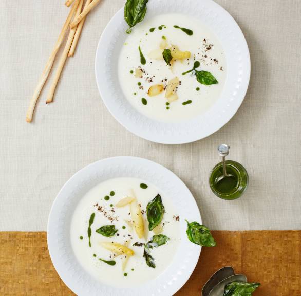 Spargelcremesuppe in zwei Suppentellern getoppt mit gebratenen Spargelstücken und Basilikumöl