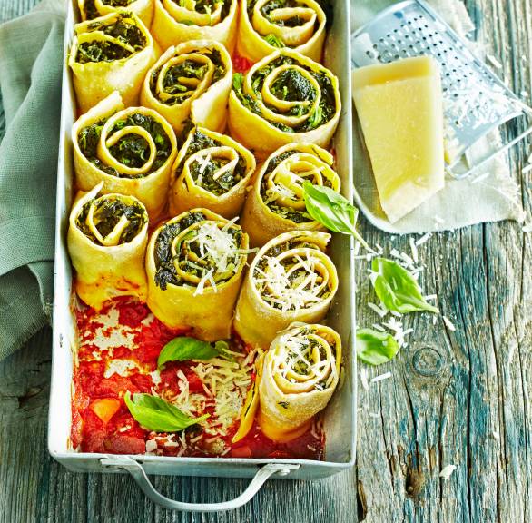 Spinat-Lasagne-Röllchen aufrecht in einer Auflaufform in Tomatensoße mit Parmesan bestreut