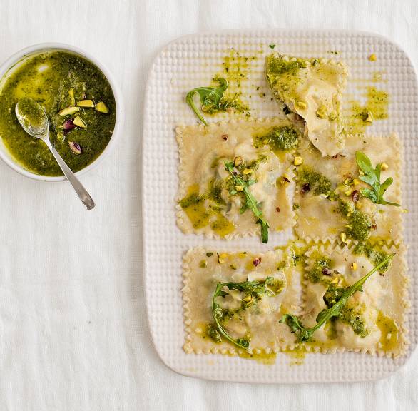 Selbst gemachte Tortelli gefüllt mit Lachs, Ricotta, Rucola und Pistazien auf einem Holzbrett, daneben Pesto