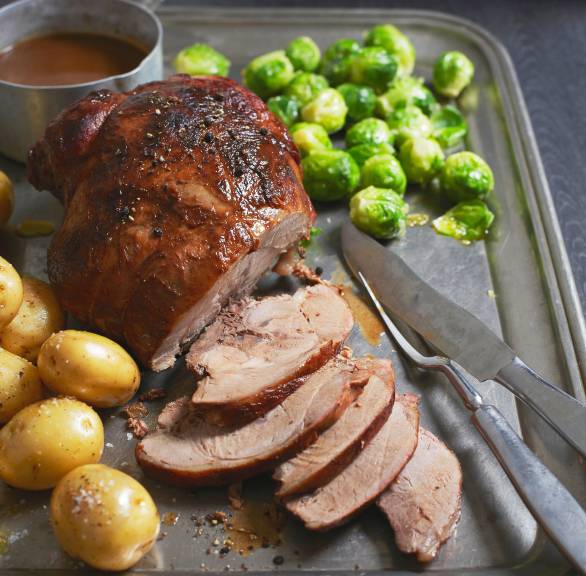 Italienischer Wildschweinbraten angeschnitten auf einer Servierplatte, daneben Kartoffeln, Rosenkohl und Soße