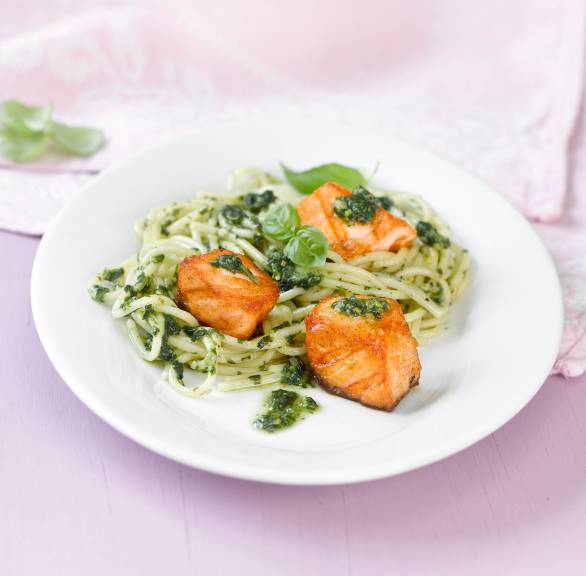Spaghetti auf einem Teller getoppt von grünem Pesto und gebratenen Lachsstücken, daneben Zitronenviertel
