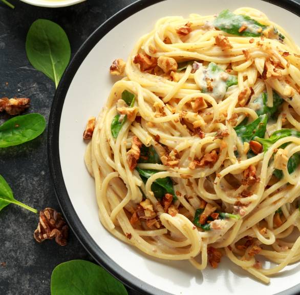 Spaghetti in Sahnesoße mit Gorgonzola und Spinat getoppt von Nüssen auf einem Pastateller