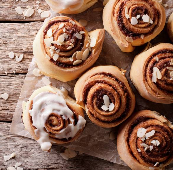 Mehrere selbst gebackene Mandelschnecken aus Hefeteig mit Zimt auf Backpapier, einige mit Glasur und Mandelblätchen verziert