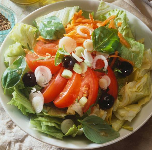 Gemischter italienischer Salat in einem tiefen Teller, daneben Olivenöl in einer Karaffe