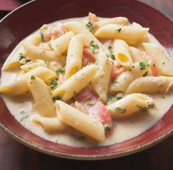 Pasta mit Lachs und Sahnesoße auf einem tiefen Teller, daneben ein Glas Rotwein