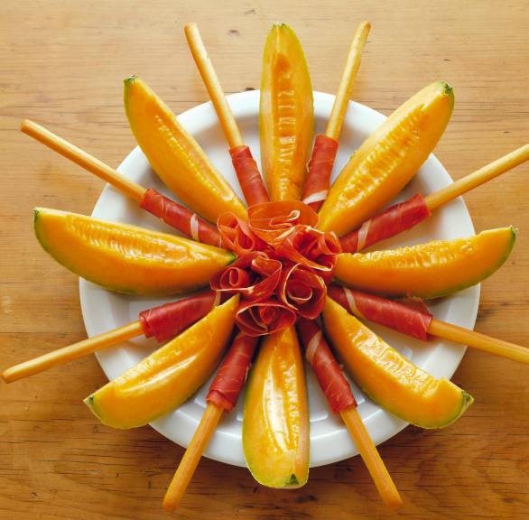 Melonenstücke mit Schinken und Grissini sternförmig auf einem Teller angerichtet