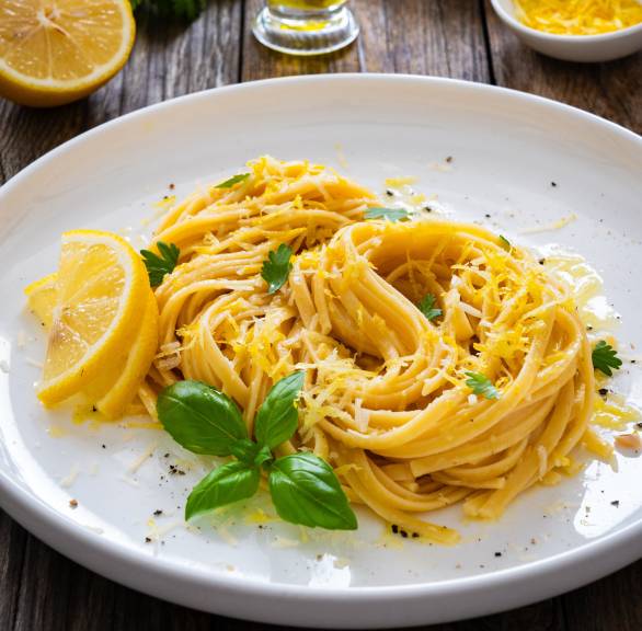 Pasta al limone Spaghetti auf einem Teller angerichtet, daneben Zitronenviertel und Olivenöl