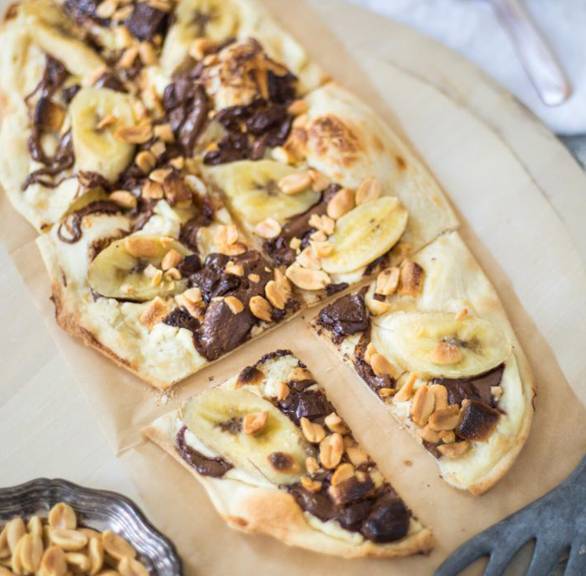Schoko-Bananen-Flammkuchen angeschnitten auf einem Backblech getoppt mit Erdnusskernen