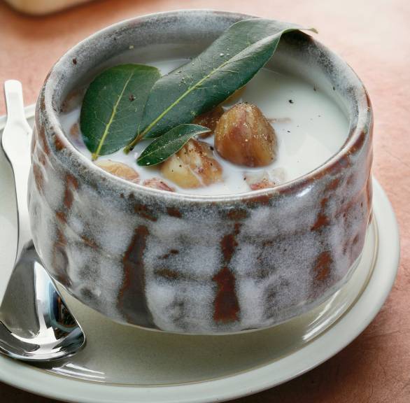 Maronensuppe in einer handgeformten Suppenschale auf einem Holztisch, daneben Maronen