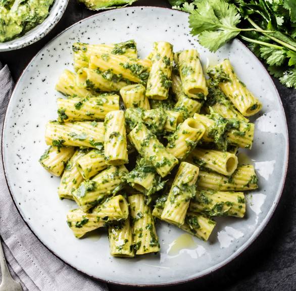 Avocado Pasta auf einem Teller, daneben eine halbierte Avocado