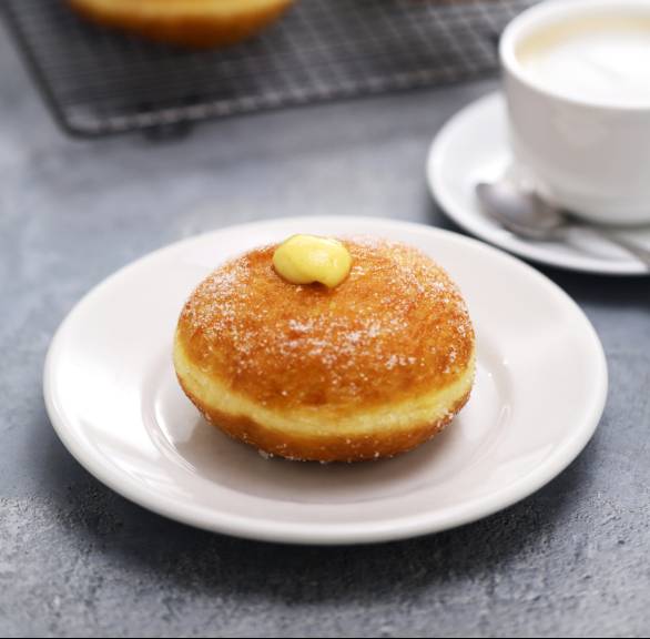Mehrere Bomboloni auf einem Kuchengitter, davor eines mit Creme gefüllt auf einem Teller