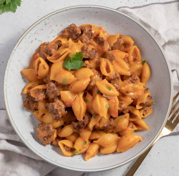 Cheeseburger Pasta in einem tiefen Teller, daneben frische Kräuter