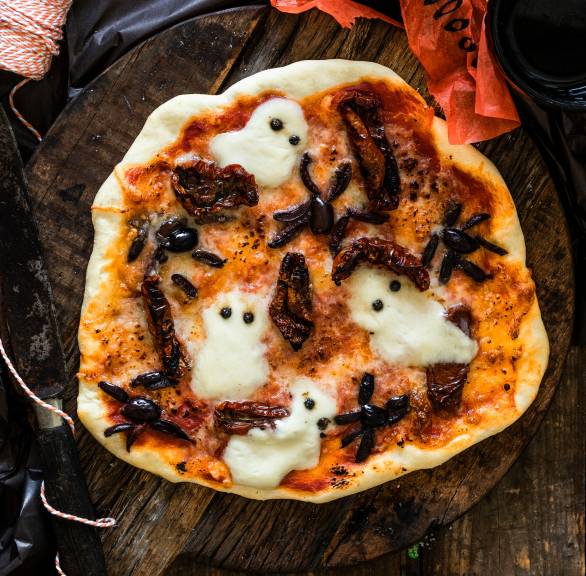 Halloween-Pizza mit Mozzarella-Geistern im Ganzen auf einem Holztisch