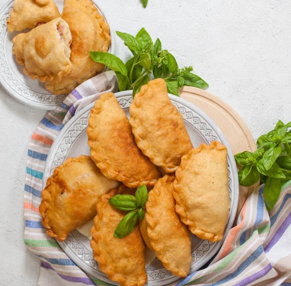 Panzerotti, gefüllte Teigtaschen auf zwei Tellern, einige aufgebrochen, sodass geschmolzener Mozzarella zu sehen ist