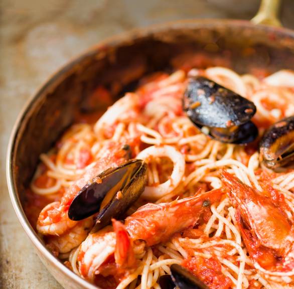 Spaghetti Frutti di Mare in einer Pfanne, daneben ein Löffel mit Tomatensauce