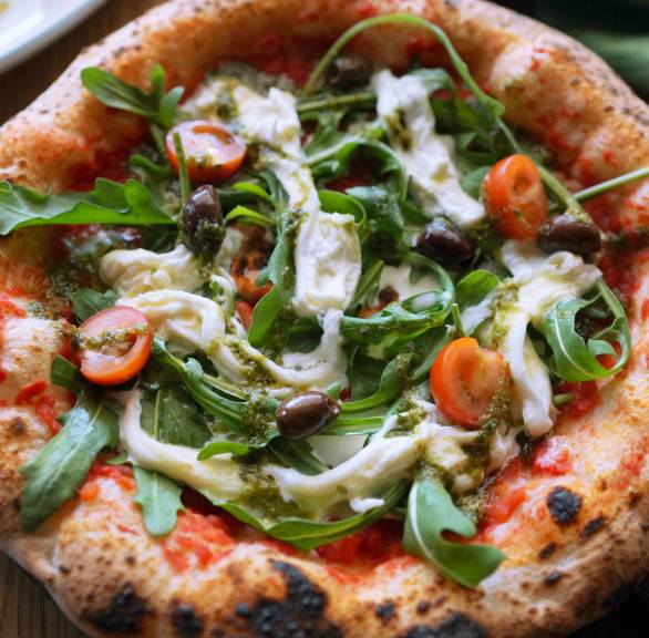 Runde Stracciatella Pizza im Ganzen auf einem teller getoppt mit Rucola