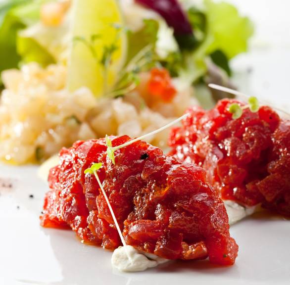 Rinder-Tartar in zwei Klecksen angeordnet auf einem Teller, dahinter Salat