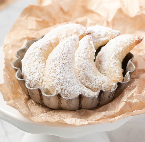 Vanillekipferl auf einer Tortenplatte, daneben Puderzucker auf einem Tisch