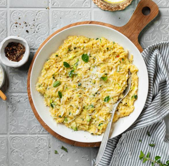 Orzotto in einem weißen Teller, daneben Parmesan und frischer Basilikum