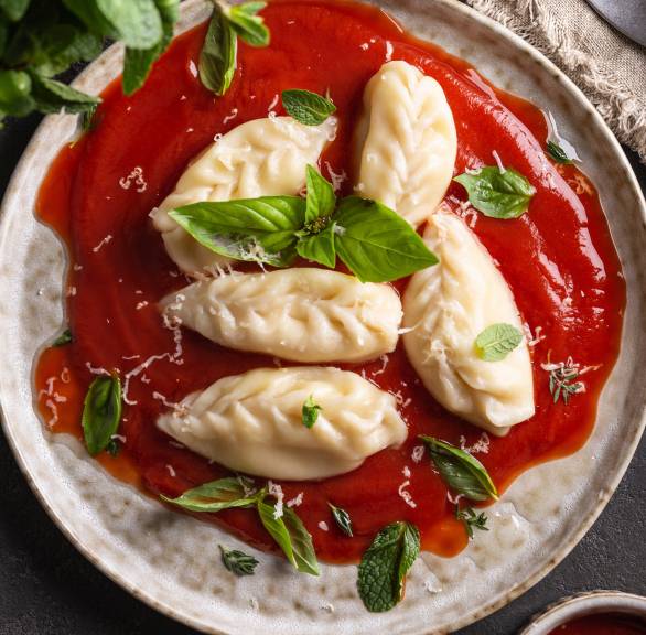 Culurgiones auf einem Teller mit Tomatensauce angerichtet und mit frischem Basilikum und Minze garniert